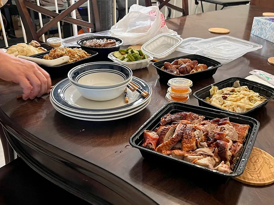 Dining table covered with takeout containers of various Cantonese BBQ dishes