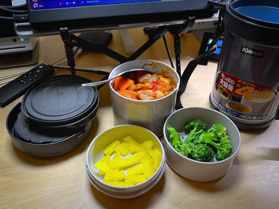 Three containers of food from a Mr Bento vacuum lunch jar. One contains yellow pickled daikon. One contains Japanese curry with rice. One contains blanched brocolli.