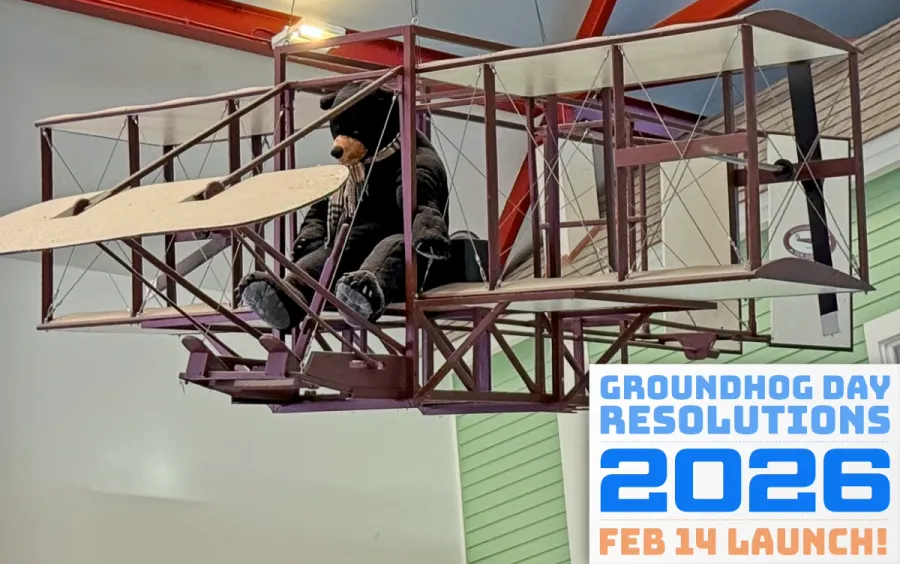 A picture of a large stuffed bear in a model of a Wright Flyer airplane in a highway rest area, suspended high from the ceiling