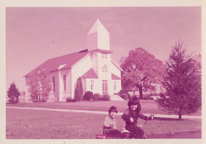 A faded photo showing two young Taiwanese-American children in front of a 150-year old American church