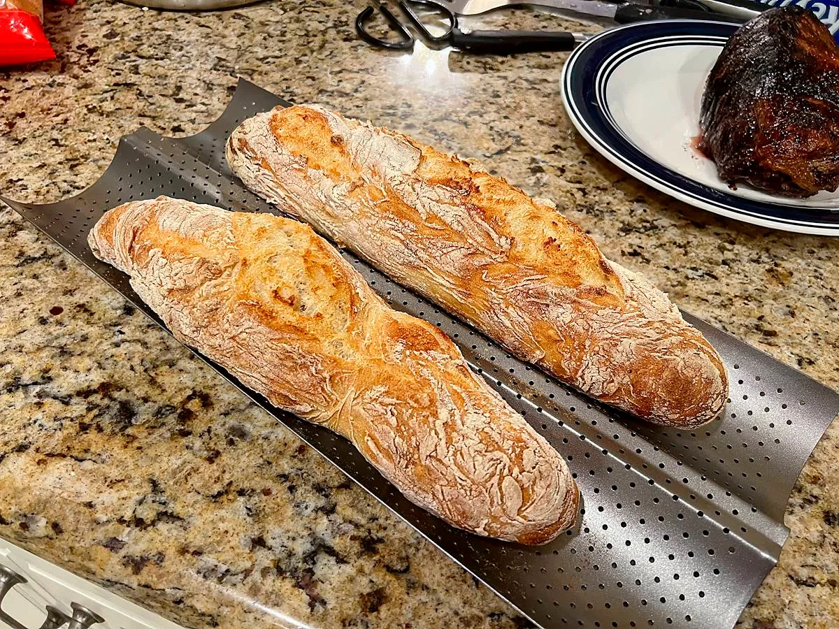 Two delicious rustic baguettes cooling on a tray on a countertop (full size image)